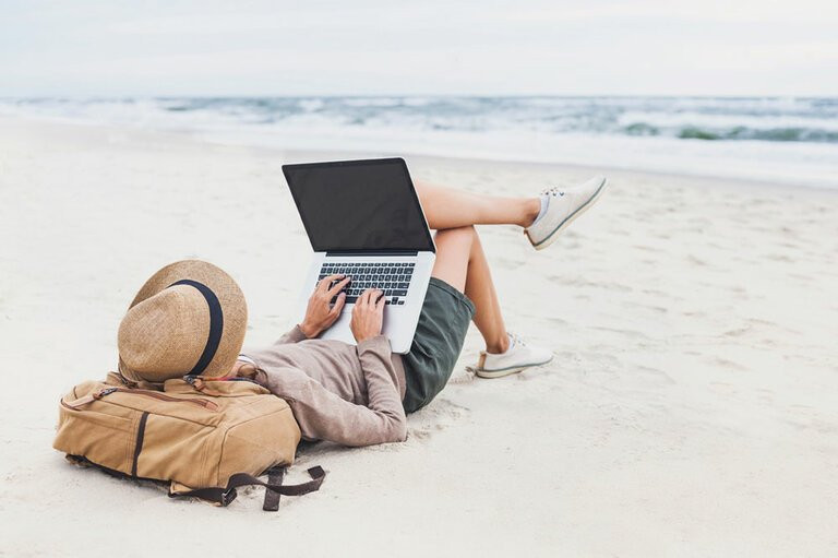 Mann mit Hut liegt gemtlich am Strand mit Laptop