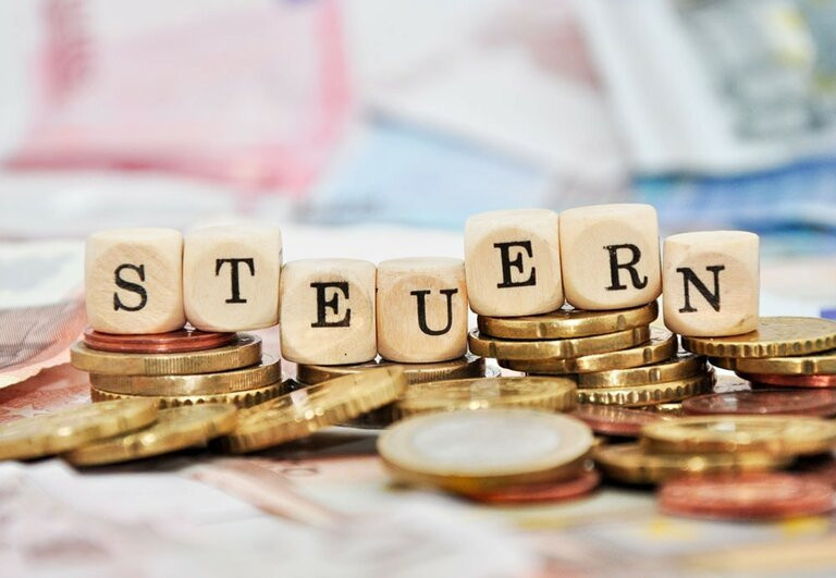 Wrfel die auf Geldstapel liegen und das Wort Steuern bilden